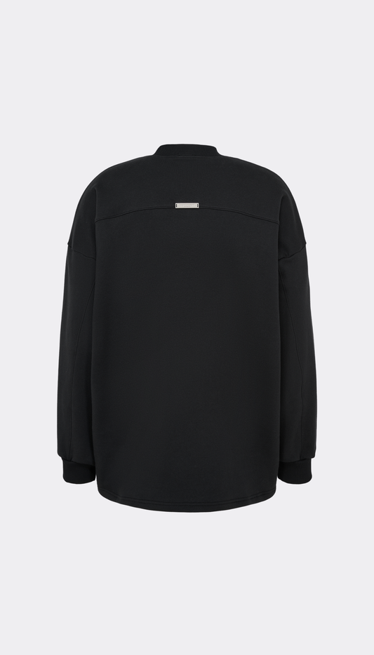A black long-sleeve pullover jacket from Haderlump shown from the back, featuring a small rectangular silver metallic accent patch near the upper back, set against a light gray background.