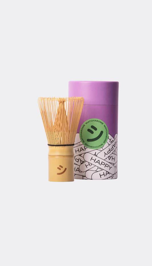 Bamboo matcha whisk and container with a smiley face label on a white background
