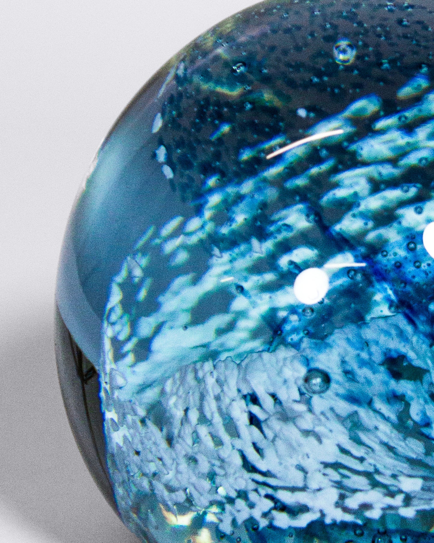 A close-up of a spherical Paper weight object with swirling blue and white patterns inside, photographed against a light gray background.
