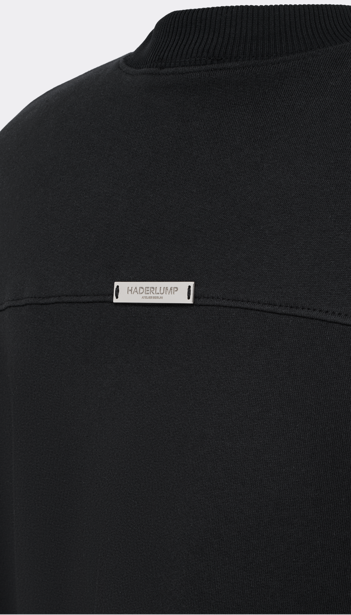 Close-up of a black crewneck sweatshirt with a silver metal Haderlump brand label.