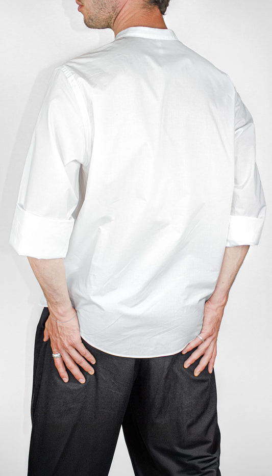 Man wearing a white SUPERMARQUE Outama shirt and black pants on a plain background